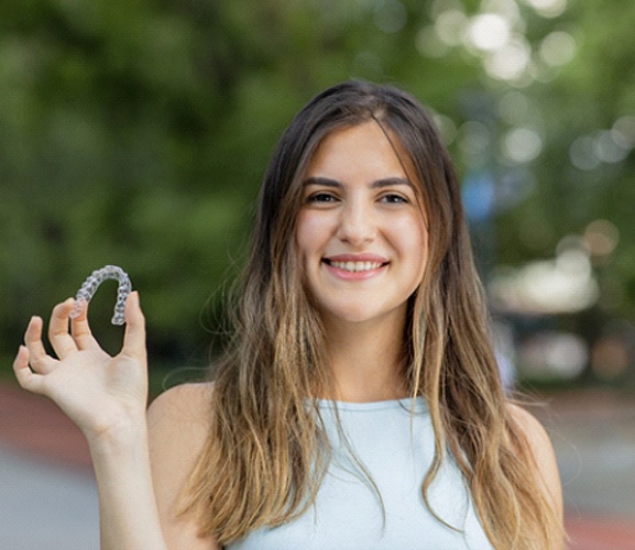 Smiling woman stands outside holding Invisalign in Dallas