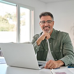 Man with glasses smiling while working on laptop
