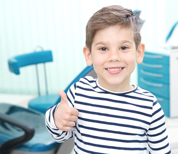 A little boy wearing a striped shirt giving a thumbs-up after a successful dental visit