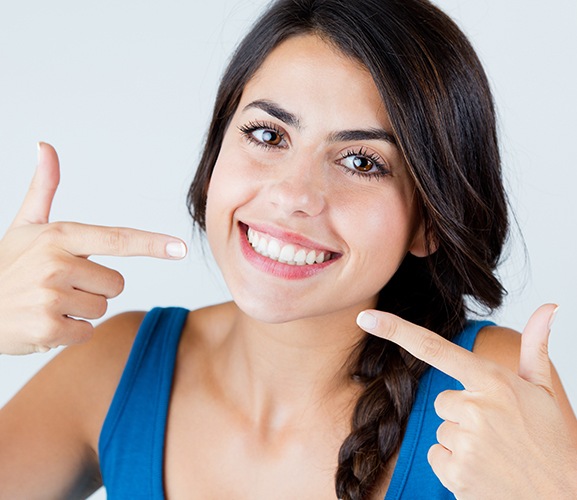 Woman with porcelain veneers pointing to her smile