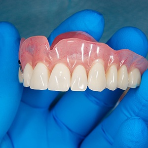 A gloved hand holding a removable denture