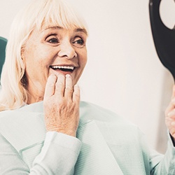 An elderly woman admiring her dentures in a hand mirror