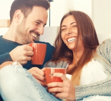 Man and woman on couch laughing and holding coffee mugs