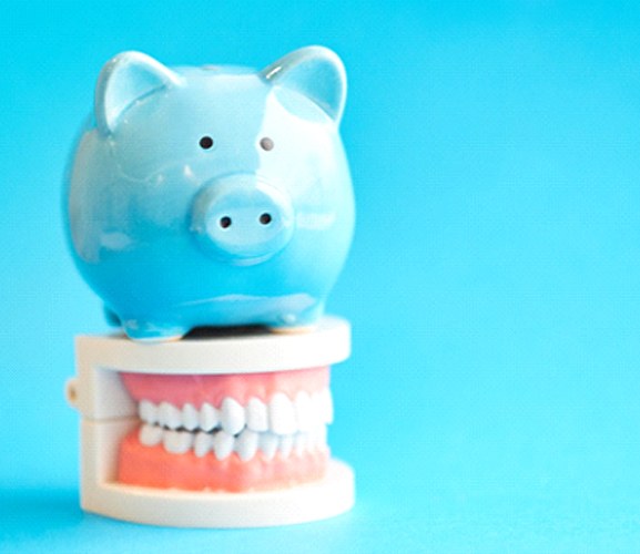 Piggy bank atop model teeth representing cost of Invisalign in Dallas