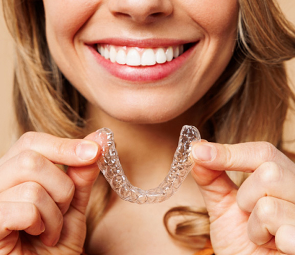 Nose-to-shoulder image of woman in orange shirt holding Invisalign smiling