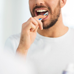 Man in white t-shirt in front of mirror brushing teeth