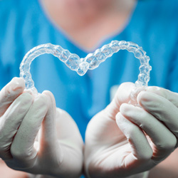 Dentist in white gloves and blue scrubs holding Invisalign in the shape of a heart