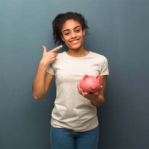 woman holding a pink piggy bank and pointing at her smile