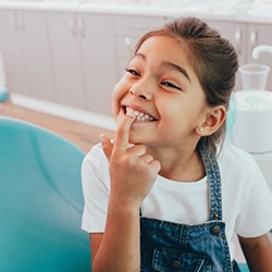 young girl in dental chair pointing to her smile 
