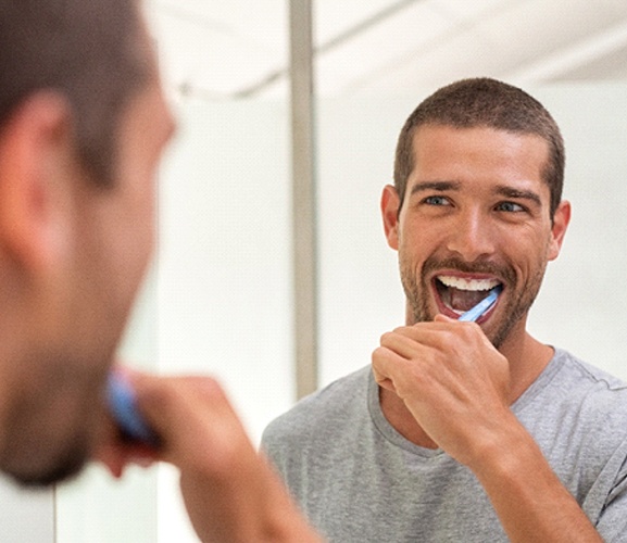 Handsome man brushing teeth to maintain results of whitening treatment