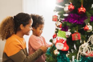 Woman and little girl smiling and decorating the tree together